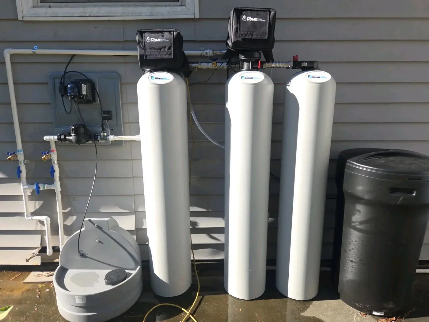 Whole-home water filtration and softening system installed outside a Sarasota, Florida home, with three treatment tanks, a salt tank and bypass valves