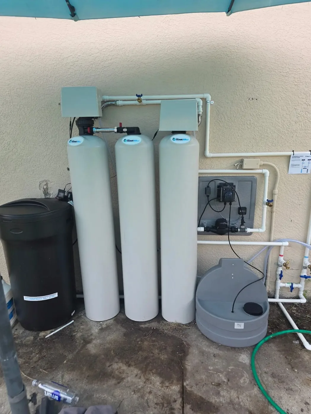 Outdoor water treatment installation at a Sarasota, Florida property, with three filtration tanks, a salt tank and a wall-mounted control panel
